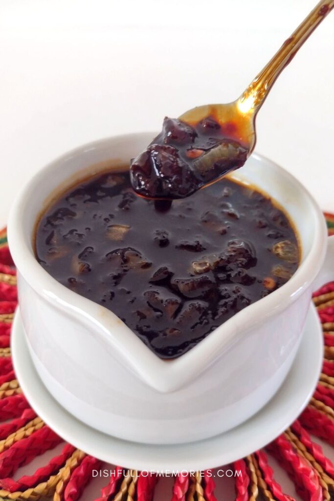 White sauce server filled with kecap manis sweet soy sauce and spoon scooping up the sauce.