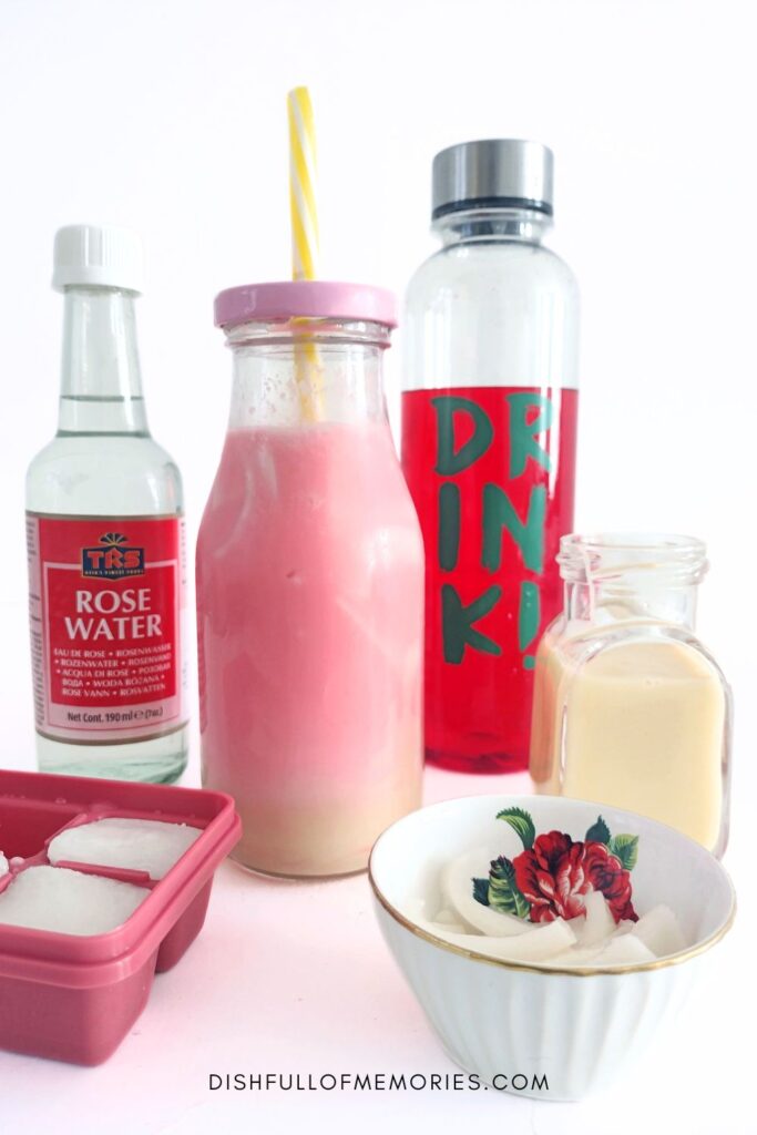 Milk bottle filled with rose milk drink, surrounded by ingredients, rose water, rose syrup, condensed milk, ice cubes.