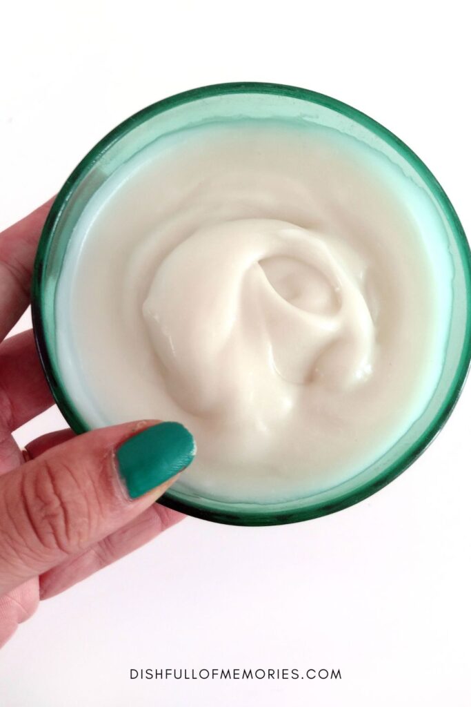 Hand holding up a green glass bowl filled with white coconut cake icing.