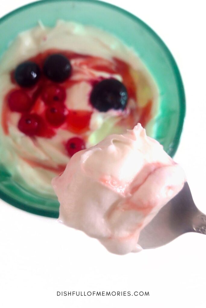 Spoon showing scoop of thick, creamy yogurt from the bowl in the background filled with Dutch hangop yogurt and red berries.