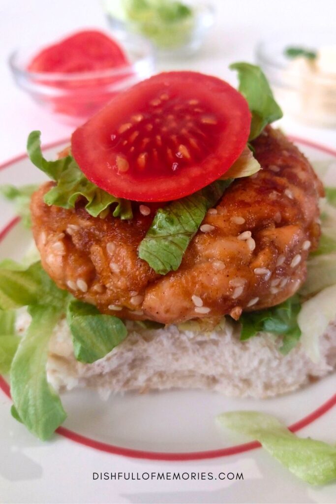 Homemade sesame salmon patty with lettuce and tomato on a burger bun.