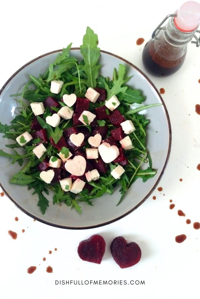 Serving plate with arugula, red beets, and feta salad Bottle of balsamic dressing and heart shaped beets and feta cheese.