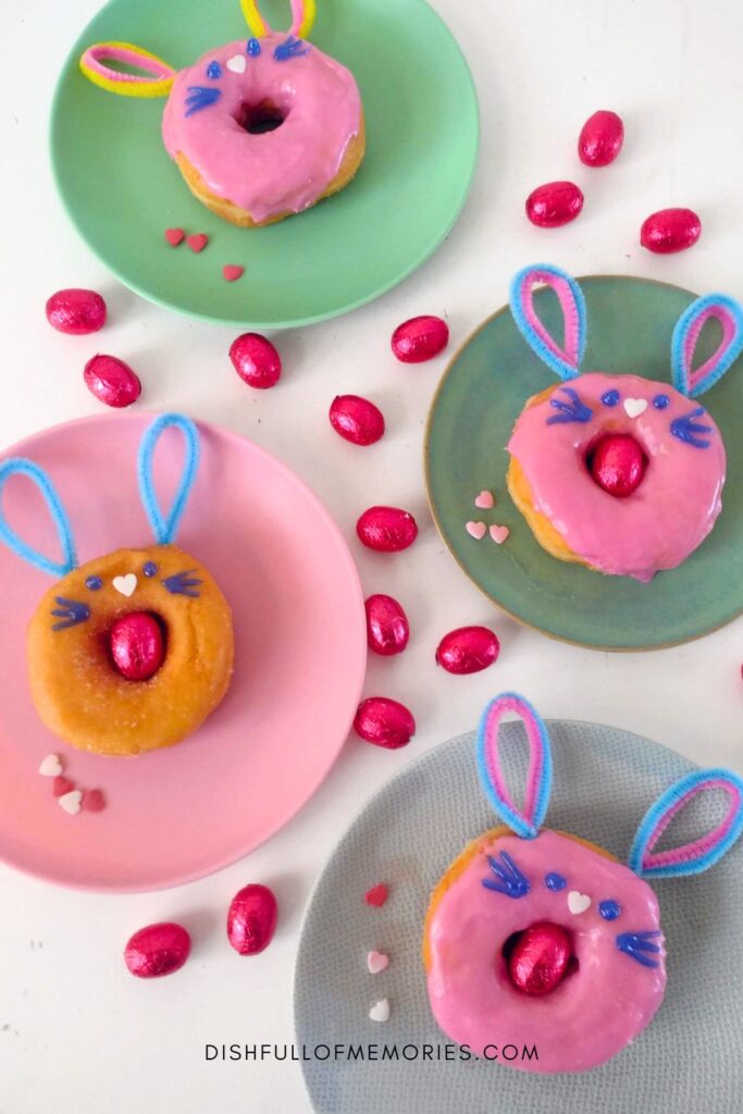 Four pastel plates with cute Easter bunny donuts and pink chocolate eggs on the table.