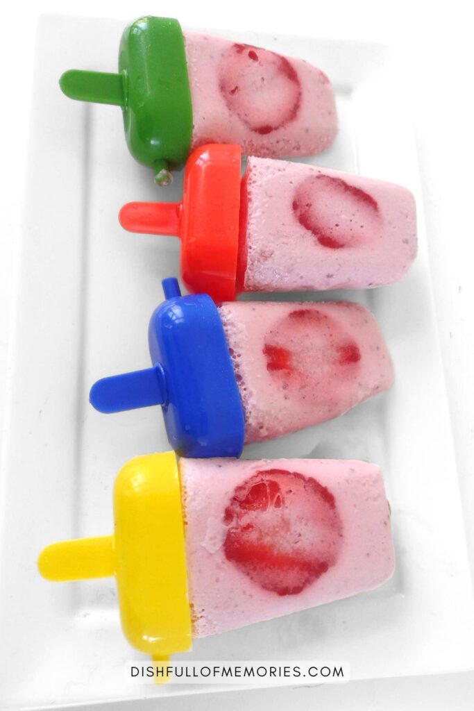 Four strawberry popsicles in rainbow molds on serving plate.