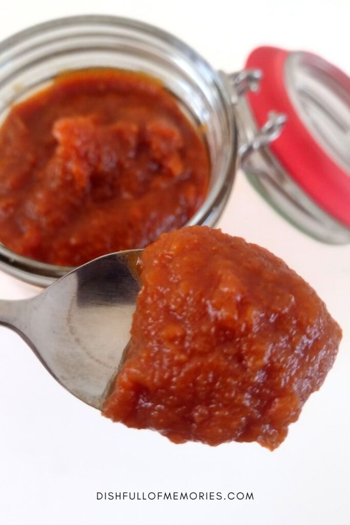 Spoon scooping up some homemade spiced pumpkin butter from a glass jar.