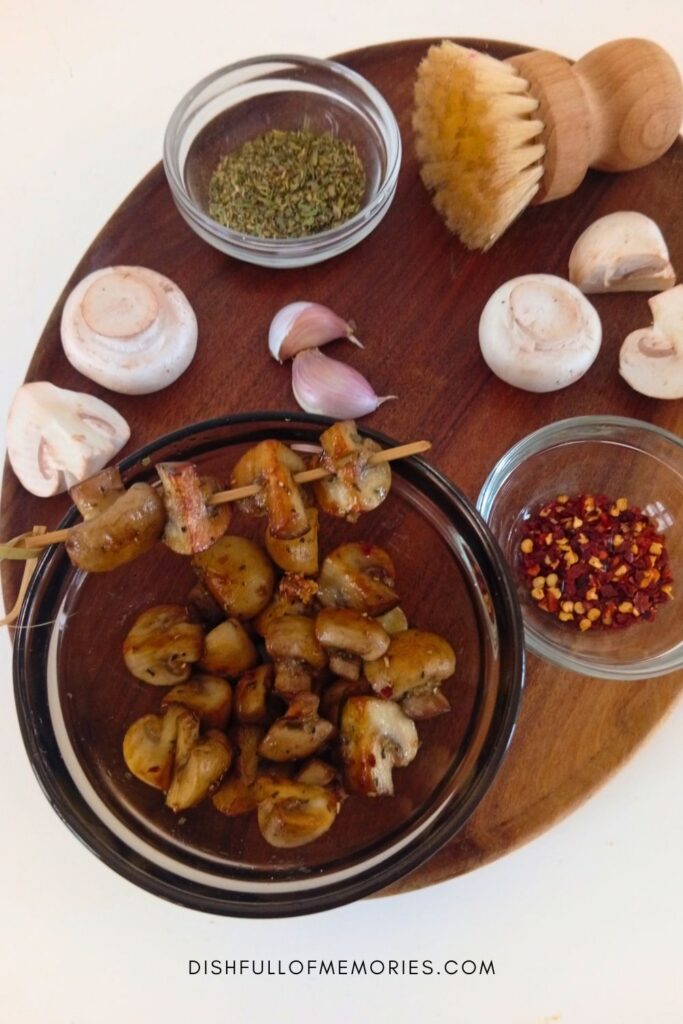 Bowl full of homemade garlic mushrooms on a round serving tray with the ingredients around it.