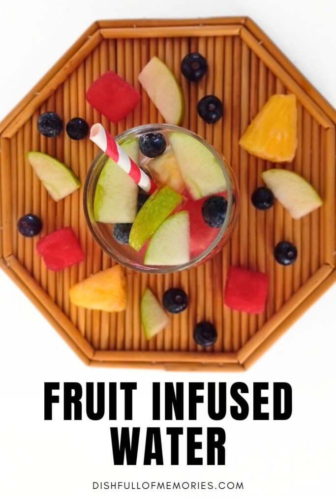 Wicker serving tray photographed from above, with bits of fruit scattered on it and a glass of fruit water in the middle. Text on image: Fruit infused water. Dish full of memories dot com.