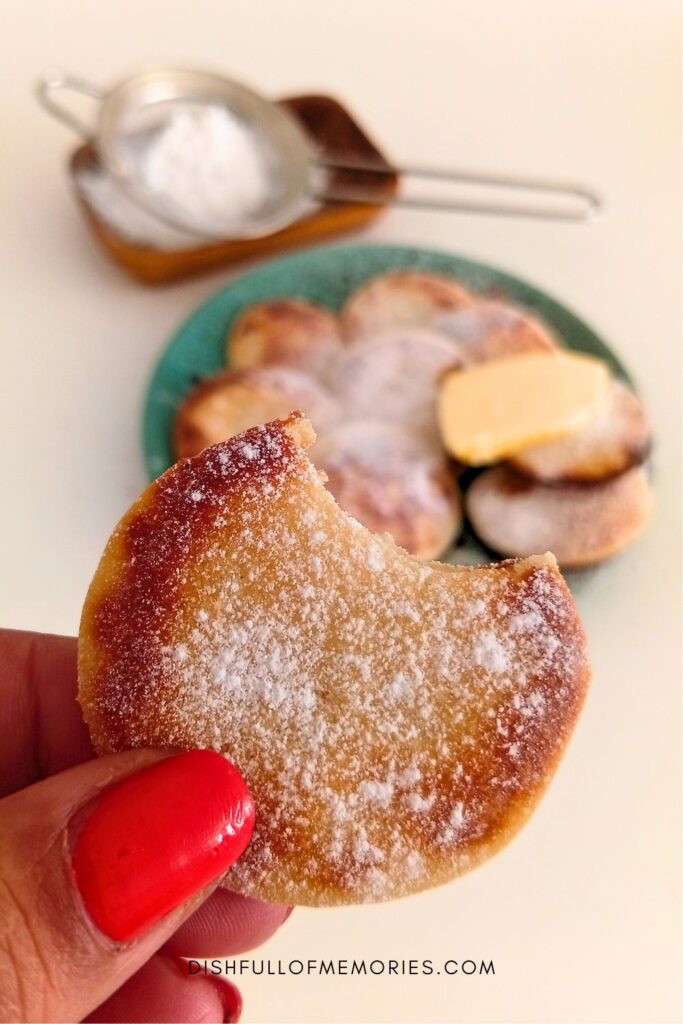 Hand holding up a Dutch poffertje mini pancake with more in the background.
