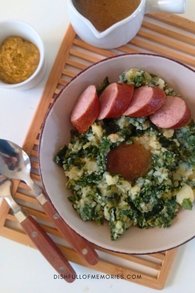Plate of Dutch Boerenkool stamppot or Kale and Potato Mash with gravy and smoked sausage.