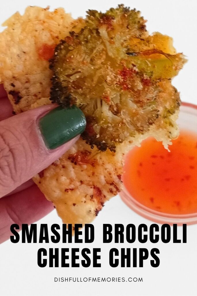 Hand holding up a homemade crispy vegetable chip with dipping sauce in the background. Text on image: Smashed broccoli cheese chips. Dish full of memories dot com.