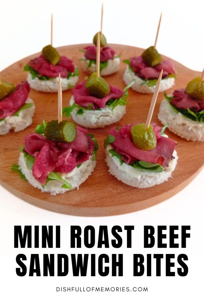 Round cutting board filled with party appetizers. Text on image: Mini roast beef sandwich bites. Dish full of memories dot com.