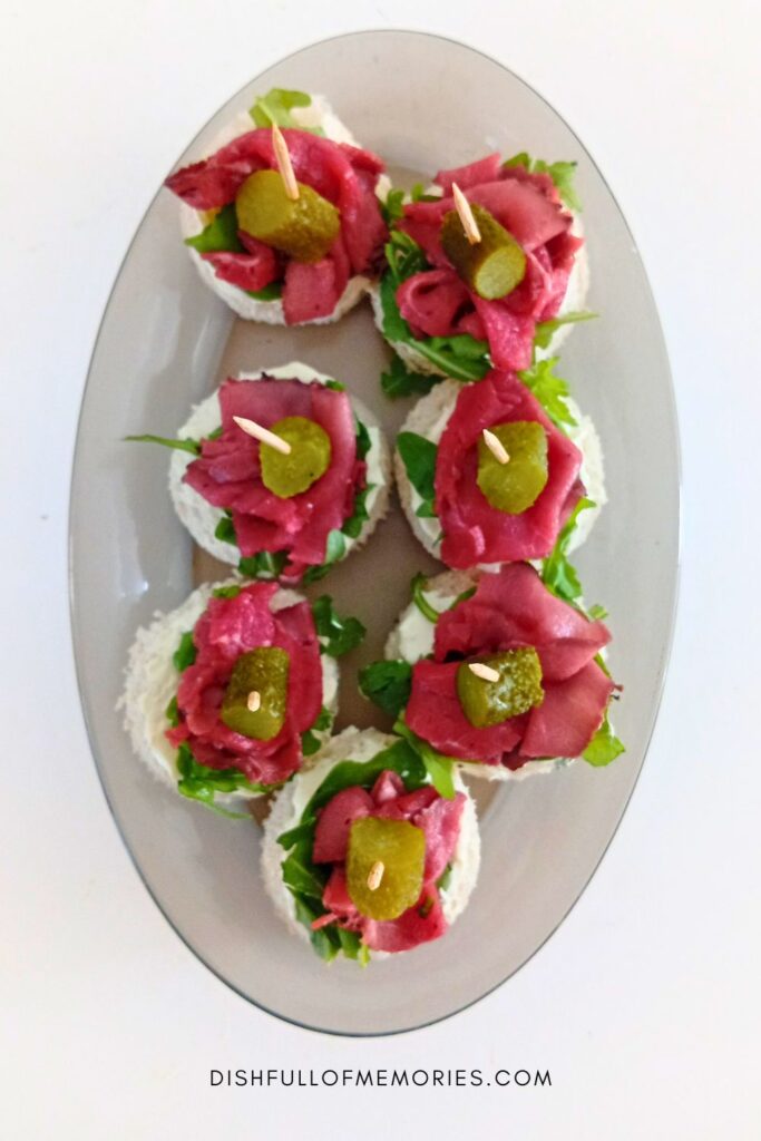 Oval serving plate with mini roast beef appetizer sandwiches.